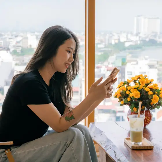 A woman using her phone by a window over the city.